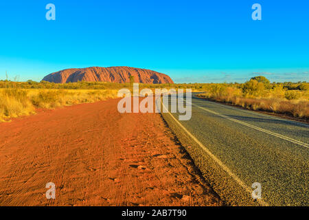 Strada che conduce a Uluru (Ayers Rock) a vivaci colori del tramonto, Outback, Uluru-Kata Tjuta National Park, UNESCO Territorio del Nord, l'Australia, il Pacifico Foto Stock