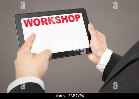 Ein Geschaeftsmann, der auf ein Tablet mit der Aufschrift 'Workshop' deutet Foto Stock