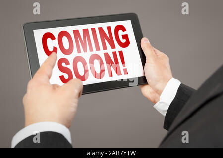 Ein Geschaeftsmann, der auf ein Tablet mit der Aufschrift " Coming soon!' deutet Foto Stock