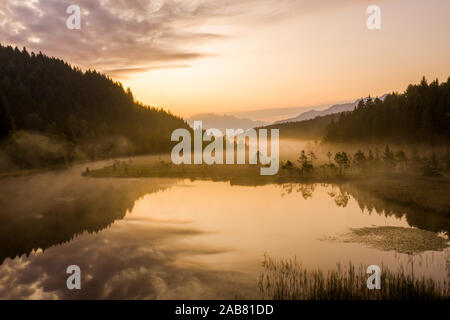 Cielo dipinto di colore arancione all'alba con misty terra di Pian di Gembro riserva naturale, vista aerea, Aprica, Valtellina, Lombardia, Italia, Europa Foto Stock