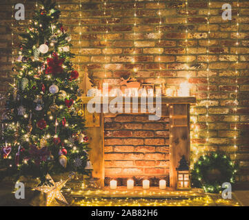 Bellissime decorazioni interne. Camino con mantelpiece in legno con le luci fairy, ornamenti fatti a mano, candele e lanterna, albero di Natale a lato, tonica, il fuoco selettivo Foto Stock