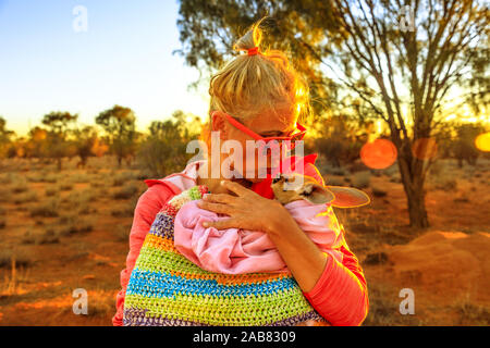 Donna turistica holding e baciare kangaroo joey alla luce del tramonto in Australian Outback Red Centre, Territorio del Nord, l'Australia, il Pacifico Foto Stock