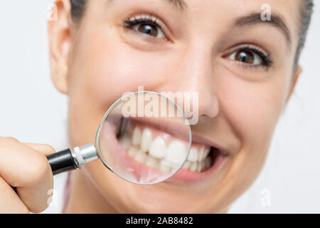 Close up divertente Ritratto di giovane ragazza che mostra denti con lente di ingrandimento. Isolato su sfondo bianco. Foto Stock