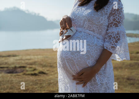 Donna incinta holding baby calzatura outdoor permanente Foto Stock