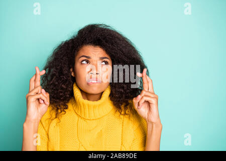 Closeup photo incredibile di pelle scura lady tenendo le dita incrociate di mordere labbra preoccupati per la scuola il test di usura a maglia gialla ponticello blu isolato teal Foto Stock