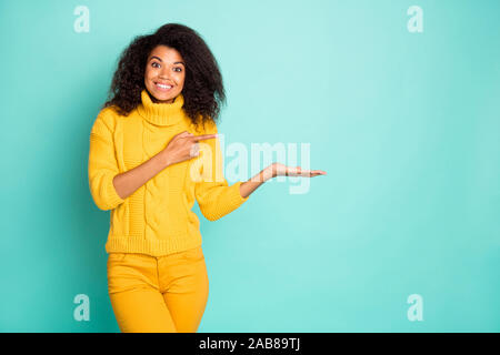 Ritratto di Nizza attraente trendy ondulata allegro-ragazza dai capelli in maglia maglione di contenimento oggetto invisibile su palm consigli advert isolate su luminose Foto Stock