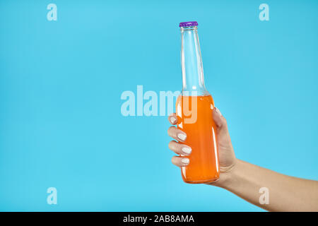 Donna con mano manicure bella bottiglia di contenimento di bevande alcoliche isolata su uno sfondo giallo Foto Stock