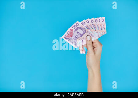 Denaro contante. Mani femminili di contenimento delle banconote in ucraino su sfondo blu. Duecento grivna banconote Foto Stock