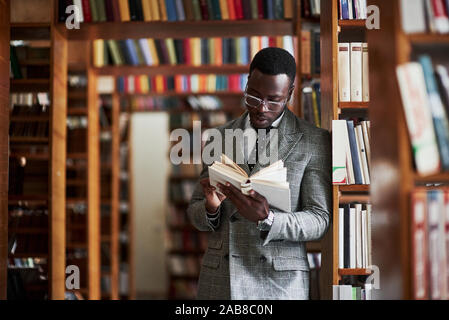 Un americano africano uomo in un business suit in piedi in una libreria in sala di lettura. Foto Stock