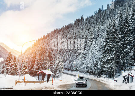 In inverno la strada alpina di paesaggio di curva con la foresta, delle montagne e del cielo blu su sfondo a bright freddo giorno di sole. Viaggio in auto famiglia viaggio. Holiday Foto Stock