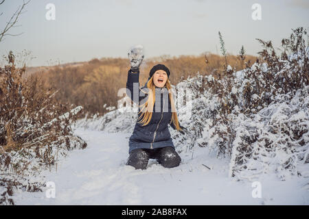 Inverno ragazza lanciando palle di neve in telecamera sorridendo felice avendo divertimento all'aperto sulla neve giornata invernale a giocare nella neve. Carino giocoso giovane donna outdoor Foto Stock