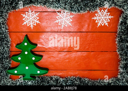 Composizione di Natale rosso sul pannello di legno con la ghirlanda di Natale e decorazioni. Composizione creativa di frontiera e di spazio copia, vista dall'alto, piatto laici. Foto Stock