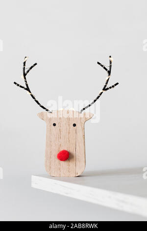 Un divertente di renne in legno di testa, con un naso rosso, su un ripiano di legno contro un sfondo bianco Foto Stock