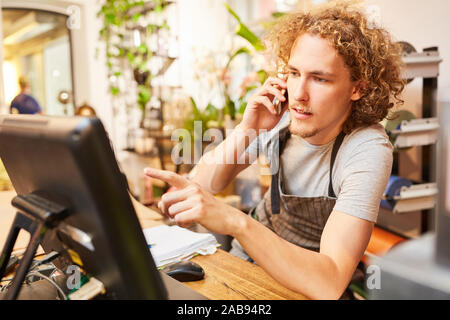 Giovani fioraio prende un ordine al telefono nel negozio di fiori Foto Stock