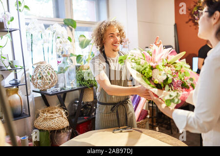 Fiorista in fiore shop vende un colorato bouquet di fiori per il cliente Foto Stock