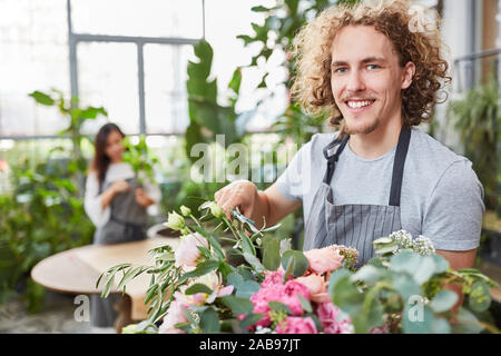 Sorridente fioraio di giovani in formazione durante la legatura bouquet Foto Stock