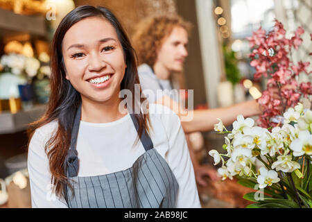 Sorridente donna asiatica come fioraio in formazione in negozio di fiori Foto Stock