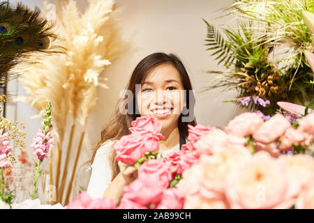 Donna asiatica come un fioraio con molte rose nel negozio di fiori Foto Stock