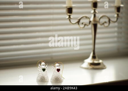 Due statuette di angeli e un candelabro stand su un bianco davanzale soleggiato, persiane orizzontale nella finestra di . Foto Stock