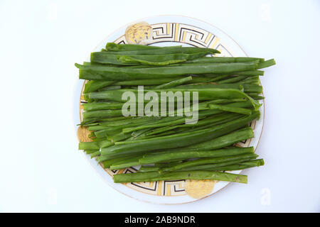 Cipolla verde su sfondo bianco . le cipolle che sono le cipolle verdi piastra bianca con alcuni tra i più piccoli di cipollotti a fette accanto ad esso su un tavolo da cucina. Foto Stock