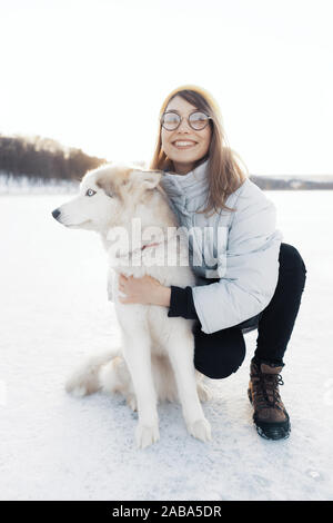 Felice giovane ragazza che gioca con siberian husky cane in winter park. Essi a piedi su un lago ghiacciato Foto Stock