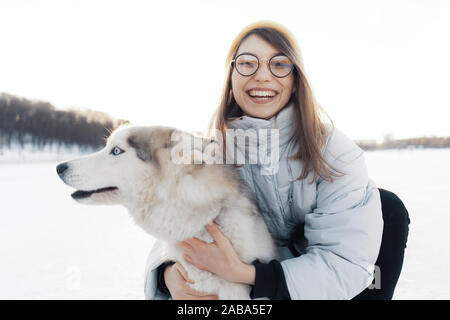 Felice giovane ragazza che gioca con siberian husky cane in winter park. Essi a piedi su un lago ghiacciato Foto Stock