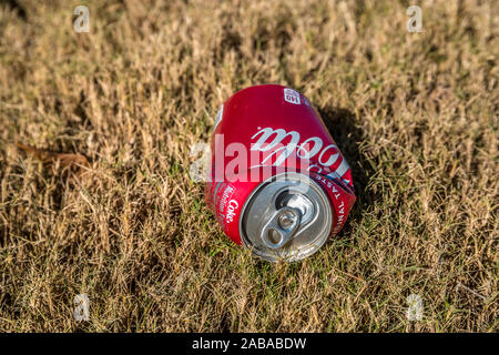 Guardando dritto dalla parte superiore della coca cola schiacciata può posa sull'erba all'esterno vuoto e scartato sul terreno in una giornata di sole in autunno Foto Stock