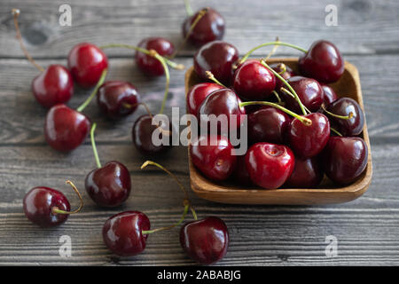 Mature ciliegie fresche in una ciotola di legno. Sfondo di cibo. Red succosa Cherry Berry su grigio Sfondo di legno. Le ciliegie in un piatto closeup. Foto Stock