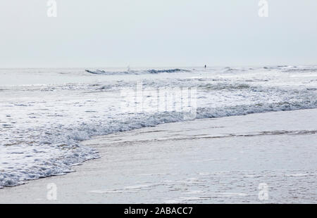 Fumoso si filtra la luce solare che colpisce onde come esse rotolano in su Ocean City Beach dove un uomo di distanza si trova sul suo stand up paddle board, Ocean City, Maryland, Foto Stock