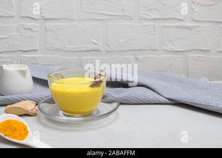 Hot bibita salutare curcuma golden latte con la curcuma in polvere di radice di zenzero, latte, il bastoncino di cannella sul cemento grigio nella tabella Foto Stock