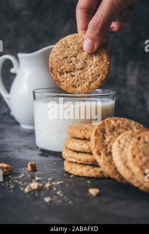 Donna di immersione in mano un cookie in un bicchiere di latte. La prima colazione dolce concetto su un sfondo marmo. Foto Stock