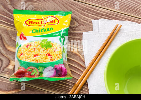 Varna, Bulgaria, 26 novembre 2019. Tagliatelle istante Rollton con sapore di pollo pack 60g vicino a bacchette e ciotola verde su un marrone tavolo in legno. Foto Stock