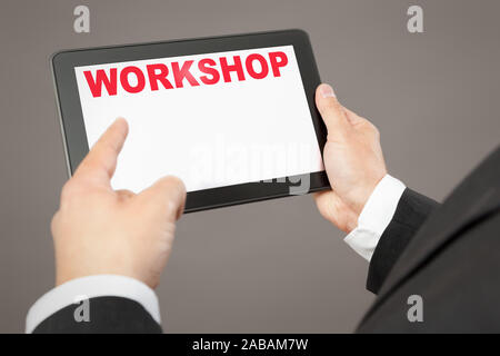 Ein Geschaeftsmann, der auf ein Tablet mit der Aufschrift 'Workshop' deutet Foto Stock