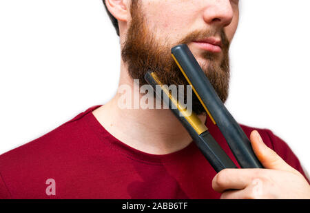 Ritratto di uomo di raddrizzare la sua barba con un raddrizzatore, lo styling della sua barba isolato su sfondo bianco Foto Stock