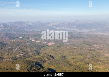 Vista da sopra di una curva highway road passando attraverso le valli e foreste con lo sfondo delle montagne e il cielo blu Foto Stock