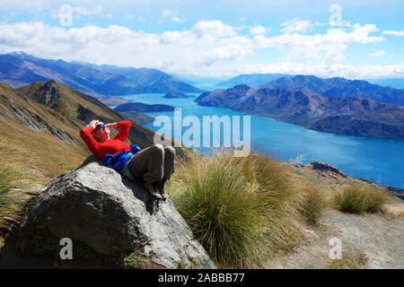 Donna sorridente giacente sulla roccia dal Lago Wanaka, Isola del Sud, Nuova Zelanda Foto Stock
