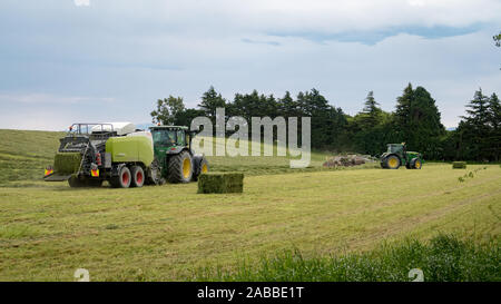 Kirwee, Canterbury, Nuova Zelanda, 26 Novembre 2019: macchine agricole al lavoro la rastrellatura fresca di erba falciata da pressare per l'inverno di alimentazione stock Foto Stock