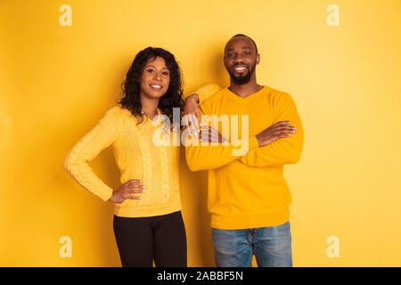 I giovani africani emotivo-american l uomo e la donna in bright abiti casual in posa su sfondo giallo. Bella giovane. Concetto di emozioni umane expession facciali, relazioni, annuncio. Con le mani incrociate. Foto Stock