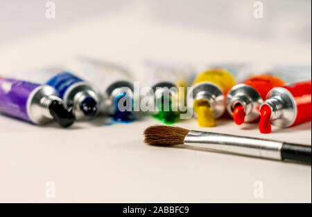 La spazzola si trova di fronte ai tubi di vernice nell'ordine dei colori dell'arcobaleno sulla tela e la vernice fluisce fuori di essi Foto Stock