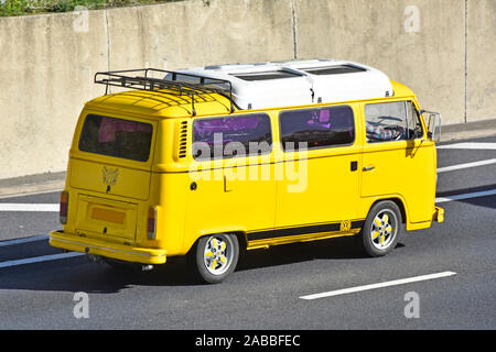 Lato & vista posteriore di vetri colorati in giallo VW Volkswagen camper van con tetto bianco & portapacchi posteriore percorrendo l autostrada M25, Essex England Regno Unito Foto Stock