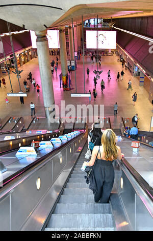 Giovani donne e altri passeggeri che discendono su scale mobili per i servizi di metropolitana treno alla stazione ferroviaria di Canary Wharf Londra Docklands Inghilterra Regno Unito Foto Stock