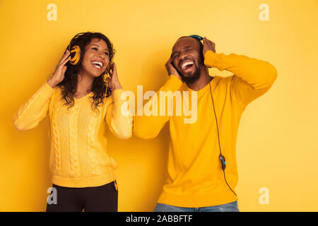 I giovani africani emotivo-american l uomo e la donna in bright abiti casual in posa su sfondo giallo. Bella giovane. Concetto di emozioni umane expession facciali, relazioni, annuncio. Ascoltare musica e cantare. Foto Stock