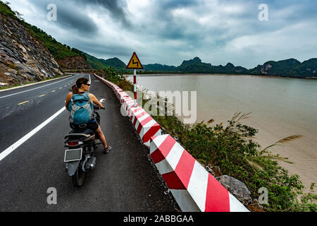 Cat Ba Island Vietnam Tourist Girl su uno scooter indossando uno zaino si ammira una splendida vista della Baia di Ha Long Foto Stock