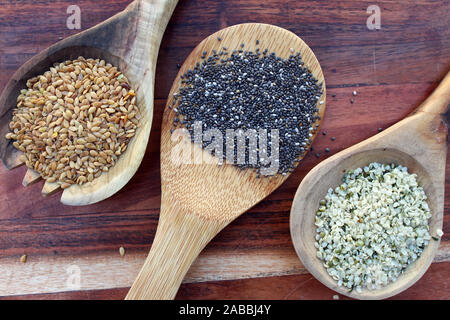 Cucchiai di legno riempita con semi di Chia, i semi di canapa cuori e golden semi di lino sullo sfondo di legno. Un concetto di cuore gentile super cibo. Foto Stock