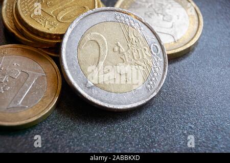 Graffiato due euro moneta di fronte a diverse altre monete euro su sfondo scuro Foto Stock
