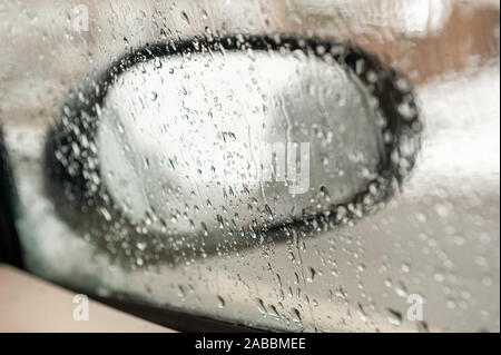 Vista di uno specchietto laterale attraverso un auto della finestra laterale coperto sotto la pioggia e la neve di fusione Foto Stock