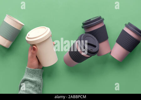 Un assortimento di bambù riutilizzabili di viaggio caffè o tè tazze o mags con isolamento in silicone.Una tazza con copy-spazio in mano femminile. Eco Friendly rifiuti zero in modo Foto Stock