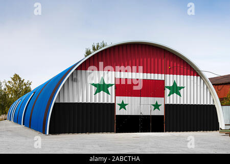 Close-up della bandiera nazionale di Siria dipinta sulla parete metallica di un grande magazzino il territorio chiuso contro il cielo blu. Il concetto di spazio di archiviazione o Foto Stock