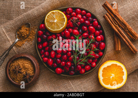 Mirtilli rossi freschi, cannella, anice, arancia, lo zucchero di canna, il rosmarino e il limone vicino, vista dall'alto su sfondo rustico Foto Stock