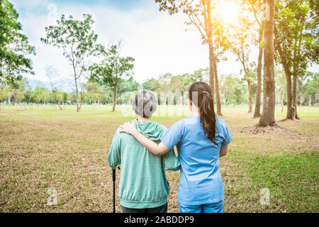 L'infermiera aiutando senior donna passeggiare intorno al parco Foto Stock